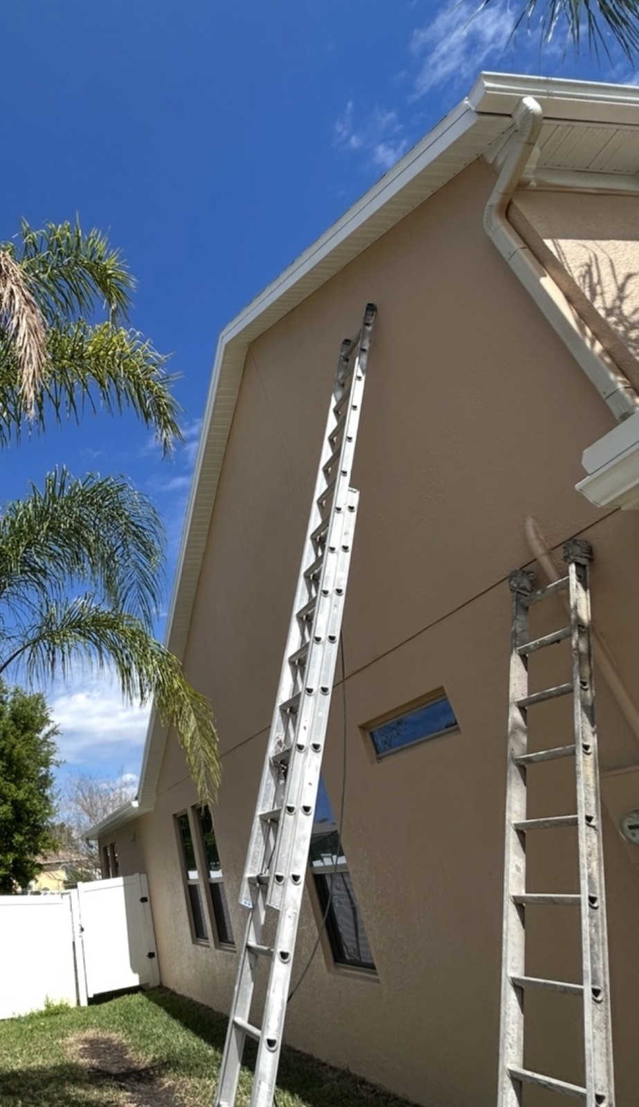 Two ladders set up against the stucco side of a two-story house during an exterior stucco and trim repaint